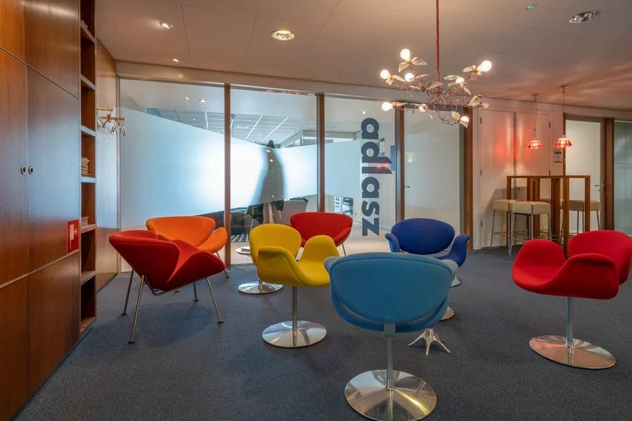 Loungehoek met donkergrijs projecttapijt en kleurrijke design fauteuils in een modern kantoor